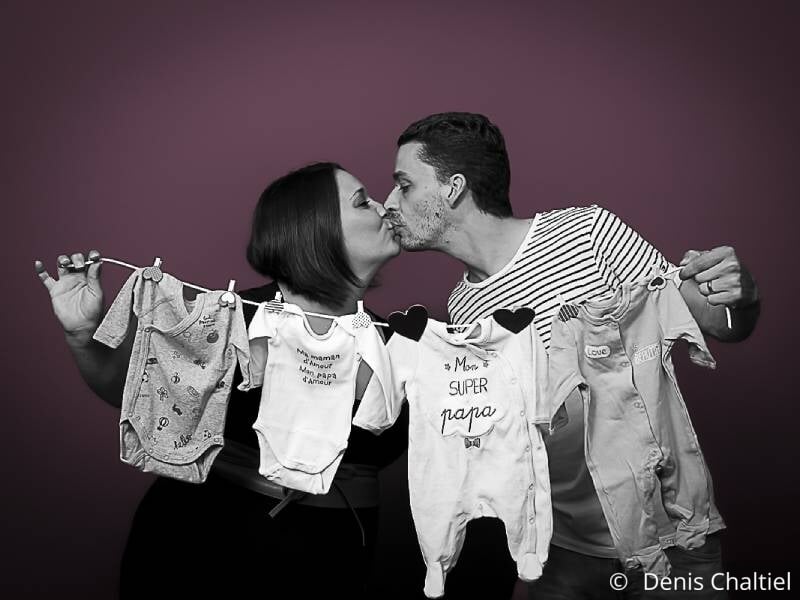 Un couple tient une corde à linge sur laquelle sont pendus des vêtements de bébé.